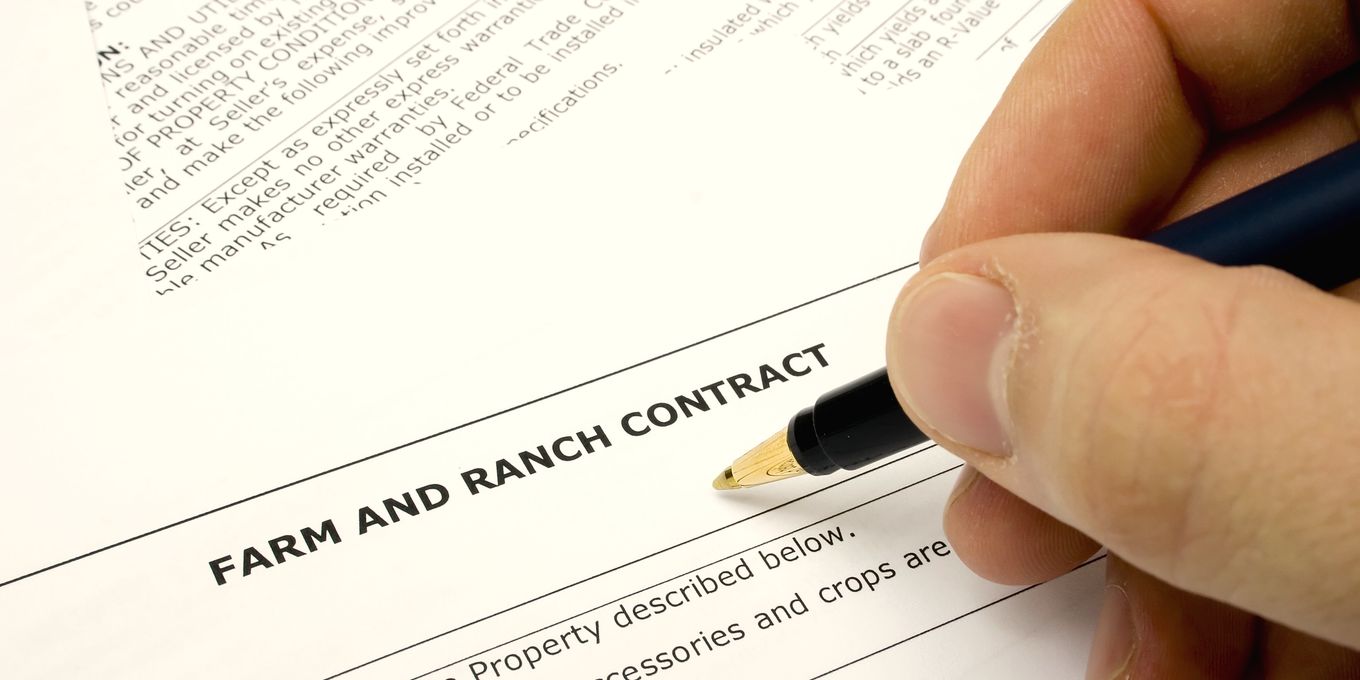 A hand signing a farm and ranch sale contract
